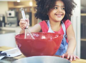 Girl stirring baking ingredients in a red bowl.