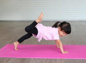 Child is on a pink yoga mat doing a yoga pose.