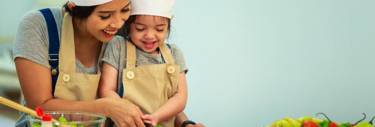 Parent and child cutting vegetables in kitchen.