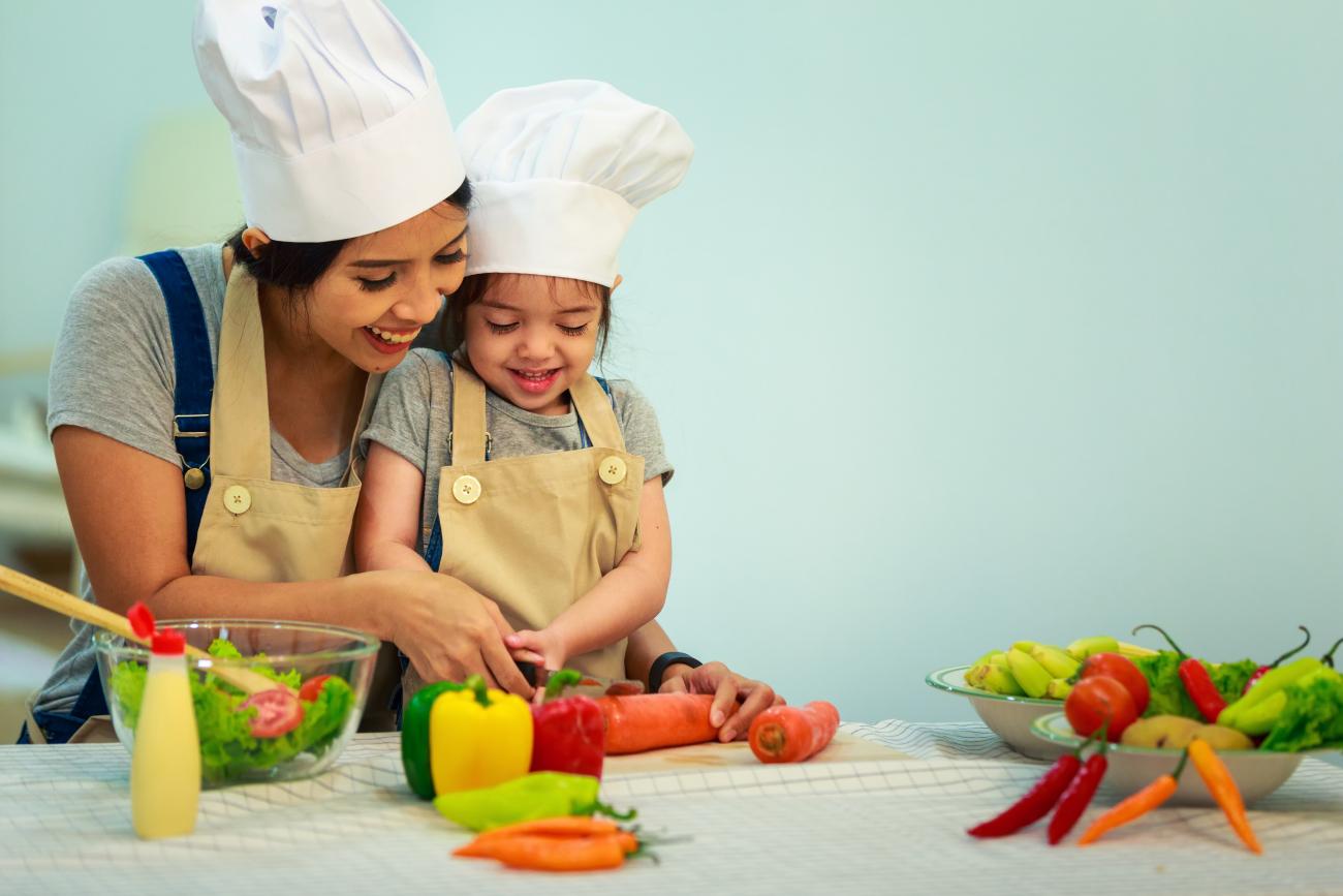 Parent and child cutting vegetables in kitchen.